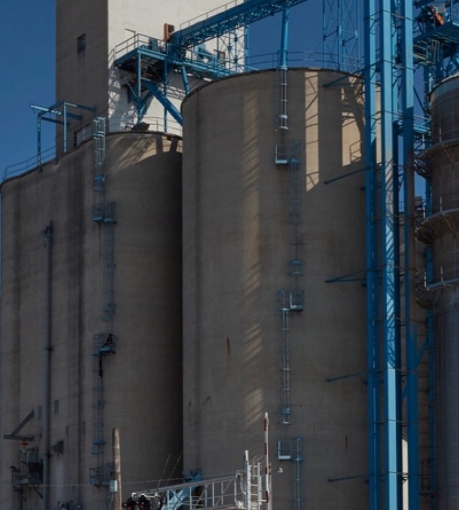 Concrete grain silos with a steel conveyor gantry against a blue sky