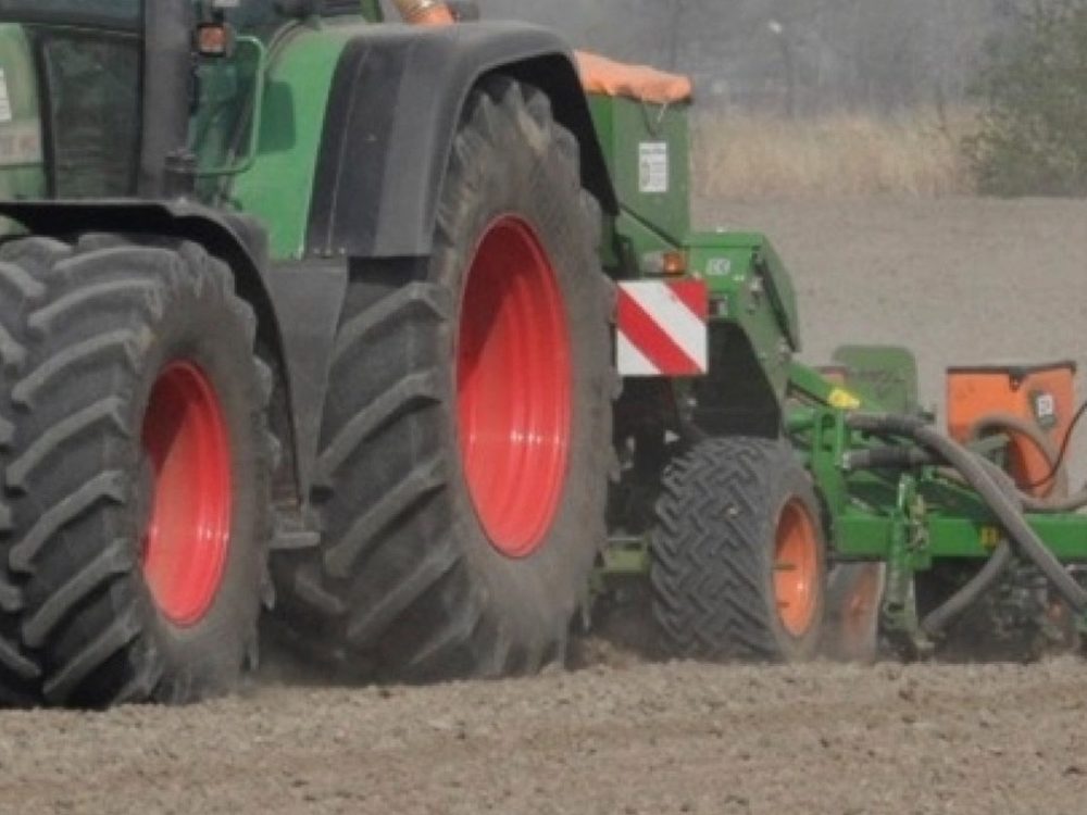 Green tractor with red wheels pulling a seed drill across a dry paddock